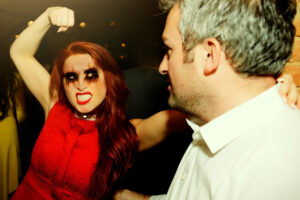a woman in a red dress pointing a fist to a man in a white shirt
