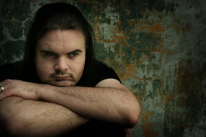 a person with long hair and a black shirt leaning against a wall
