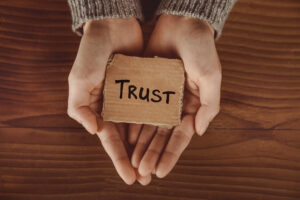 Hands making a cup shape with a brown paper with the word TRUST written