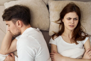 Two people are sitting on a bed and looking away from each other