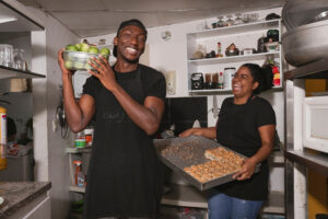 Two people standing in a kitchen holding a tray of food