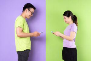 Two people standing next to each other looking at their phones