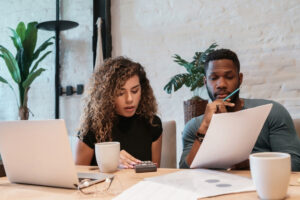 two people sitting at a table with laptops and papers