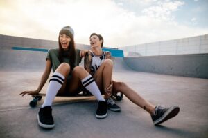 Two people sitting on a skateboard in a skate park laughing.