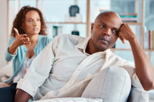 A person sitting on a couch with another person in the background