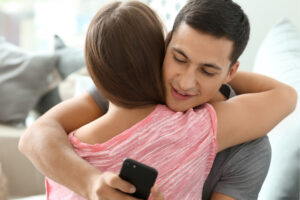 a person is hugging their partner while looking at a phone