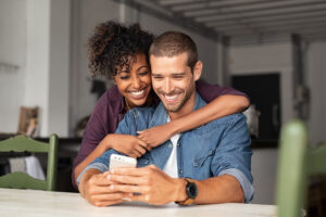 A couple clinging to each other and smiling while looking at their cell phone