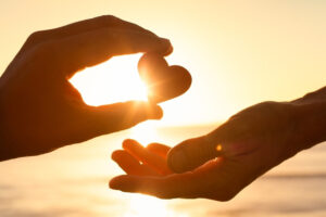 two hands holding a heart in front of the sun