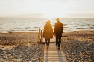 Two people walking down a boardwalk on a beach at sunset