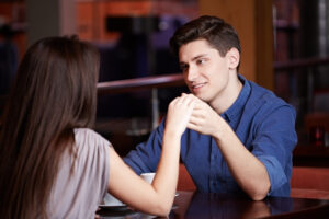 Two individuals are sitting at a table in a restaurant holding hands.