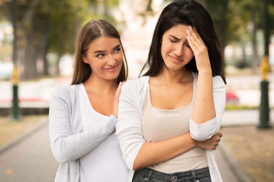 Brunette woman consoling a distressed dark-haired woman outdoors.