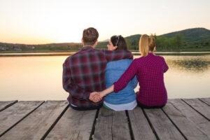 Three people sitting on a dock with their arms around each other