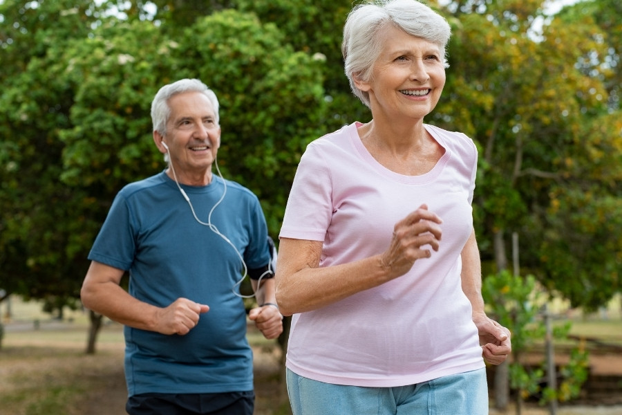 Elderly couple jogging outdoors on a park trail, smiling.
