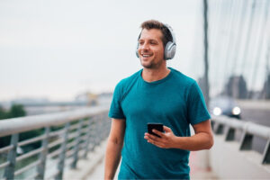 A man with a headphone and a phone jogging in the open.