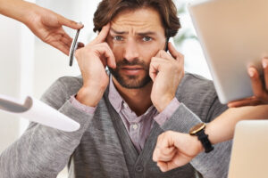 a person sitting at a desk with their hands on their head and two other people bring phones and tablet to his face.