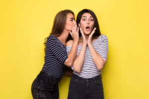 one person whispering to the other person's ear before a yellow background