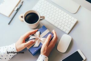 hands holding a gift box on a desk in front of a laptop and a cup of coffee