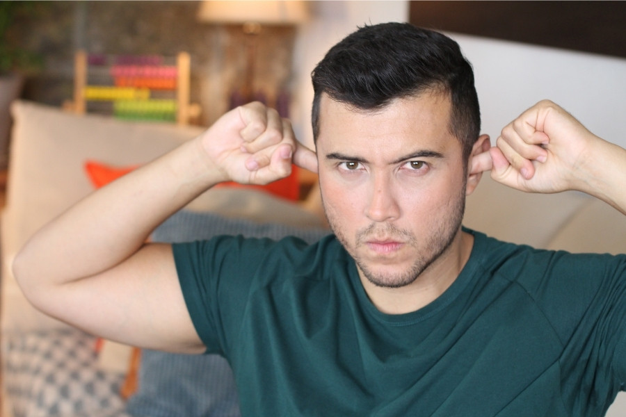 Portrait of a man plugging his ears with an annoyed expression.