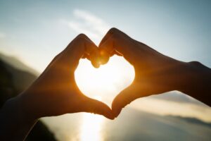 two hands making a heart shape with the sun in the background