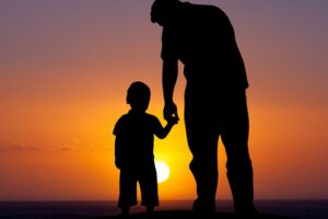 silhouette of parent and child holding hands at sunset