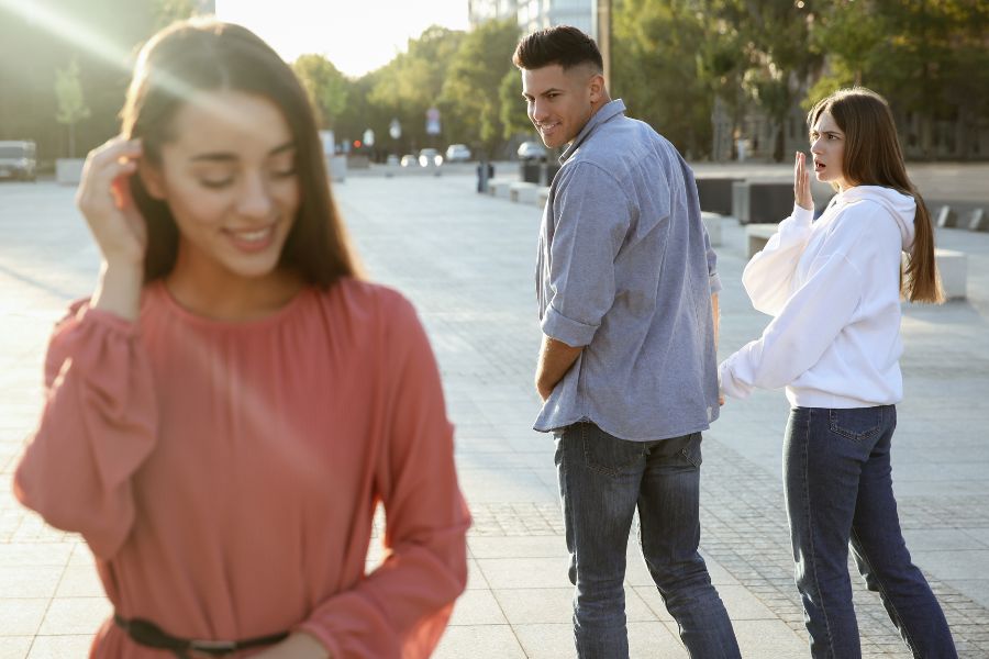 A man looking back at another woman walking away with a woman by his side down the street together