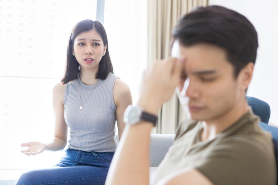 Two people sitting on a couch in a living room with the woman opening her arms in a conversation gesture