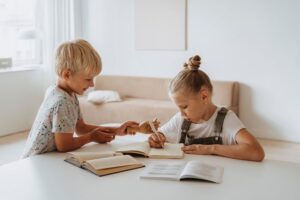two children sitting at a table with books