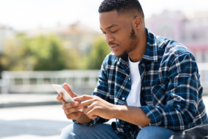 a person in a plaid shirt sitting on the ground looking at their cell phone