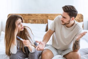 Two people sitting on a bed looking at a thermometer