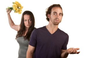 a seemingly unhappy woman raising a bouquet behind a man.