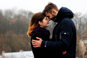 A person and another person embrace in front of a forest