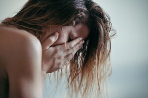 A woman holding her face in her hands with her hairs all over the head