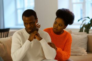 A woman holding a a man by the arm while sitting behind hin on the couch