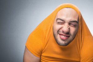 a person in an orange shirt pulled over his head and  is making a funny face