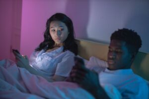 A couple on the bed both looking at their phones
