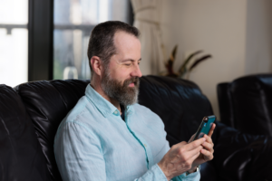 a person with a beard sitting on a couch looking at their phone