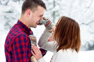 A lady playfully holding the nose of a man in the snow
