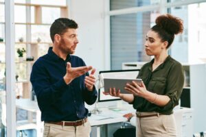 A woman showing a tablet to a man who shows her the way out with his hands in an office