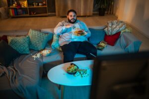 a person sitting on a couch eating food while watching tv
