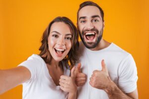 Portrait of a happy couple showing thumbs up on an orange background 